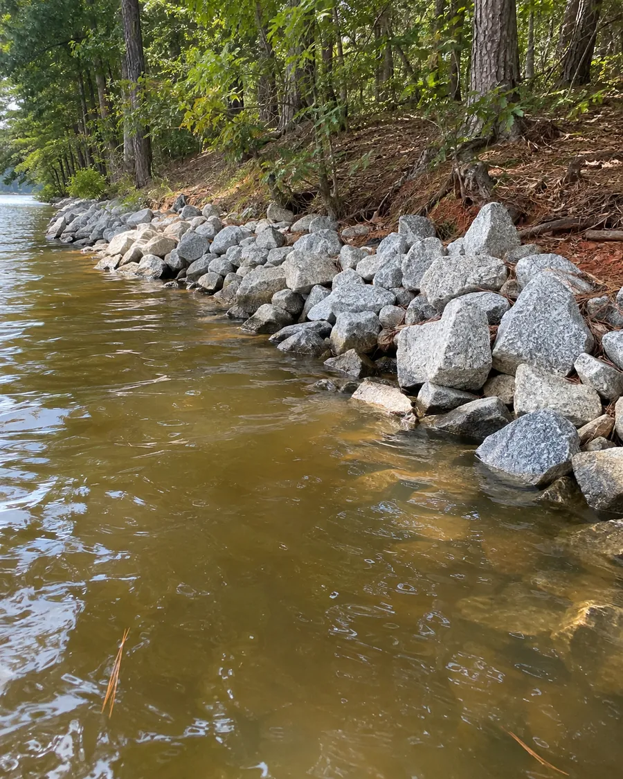 Gray riprap stone along a wooded lake bank, with the water lapping at the bottom row of rocks